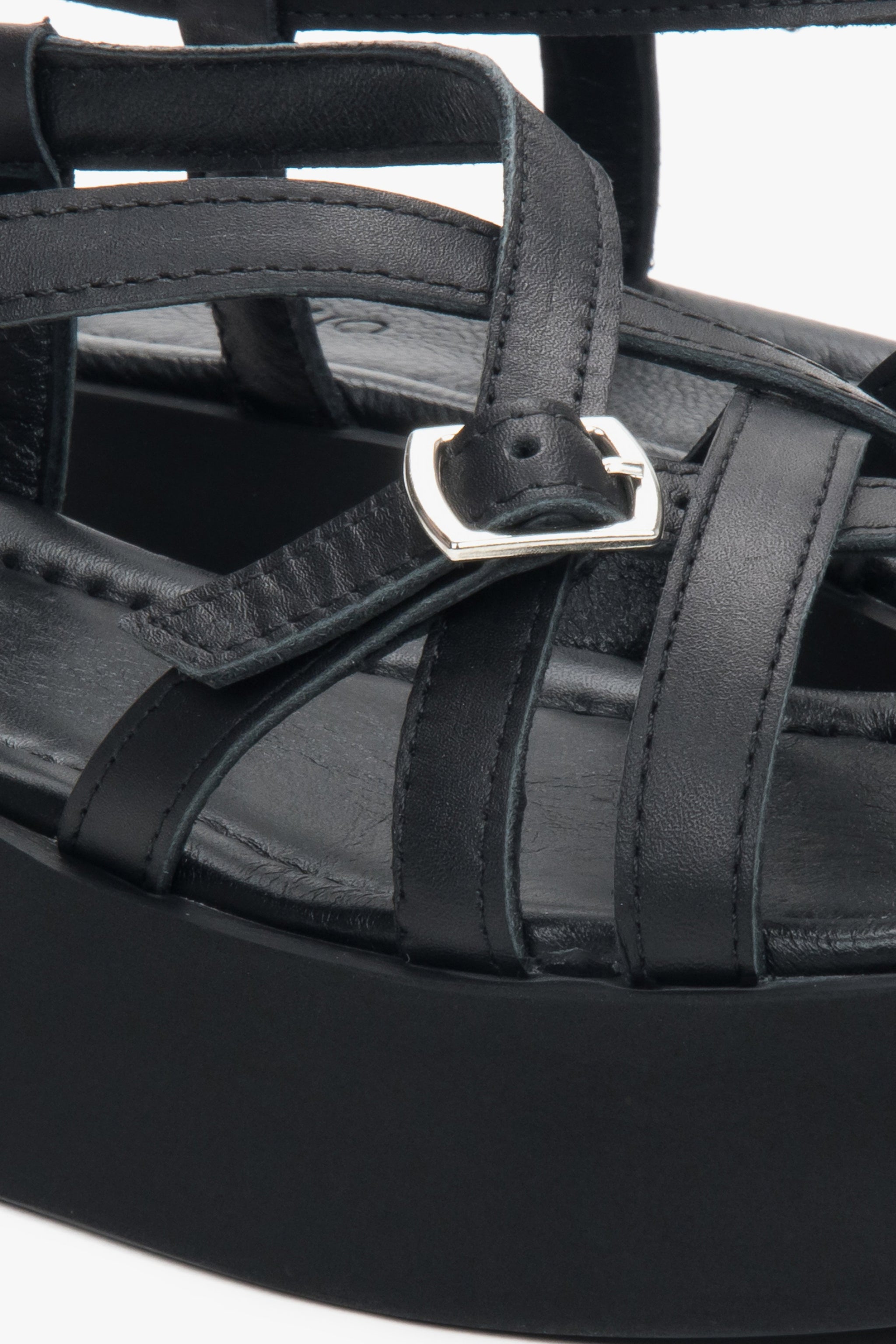 Detailaufnahme der silbernen Schnalle und der Lederriemen an den schwarzen Plateau-Sandalen