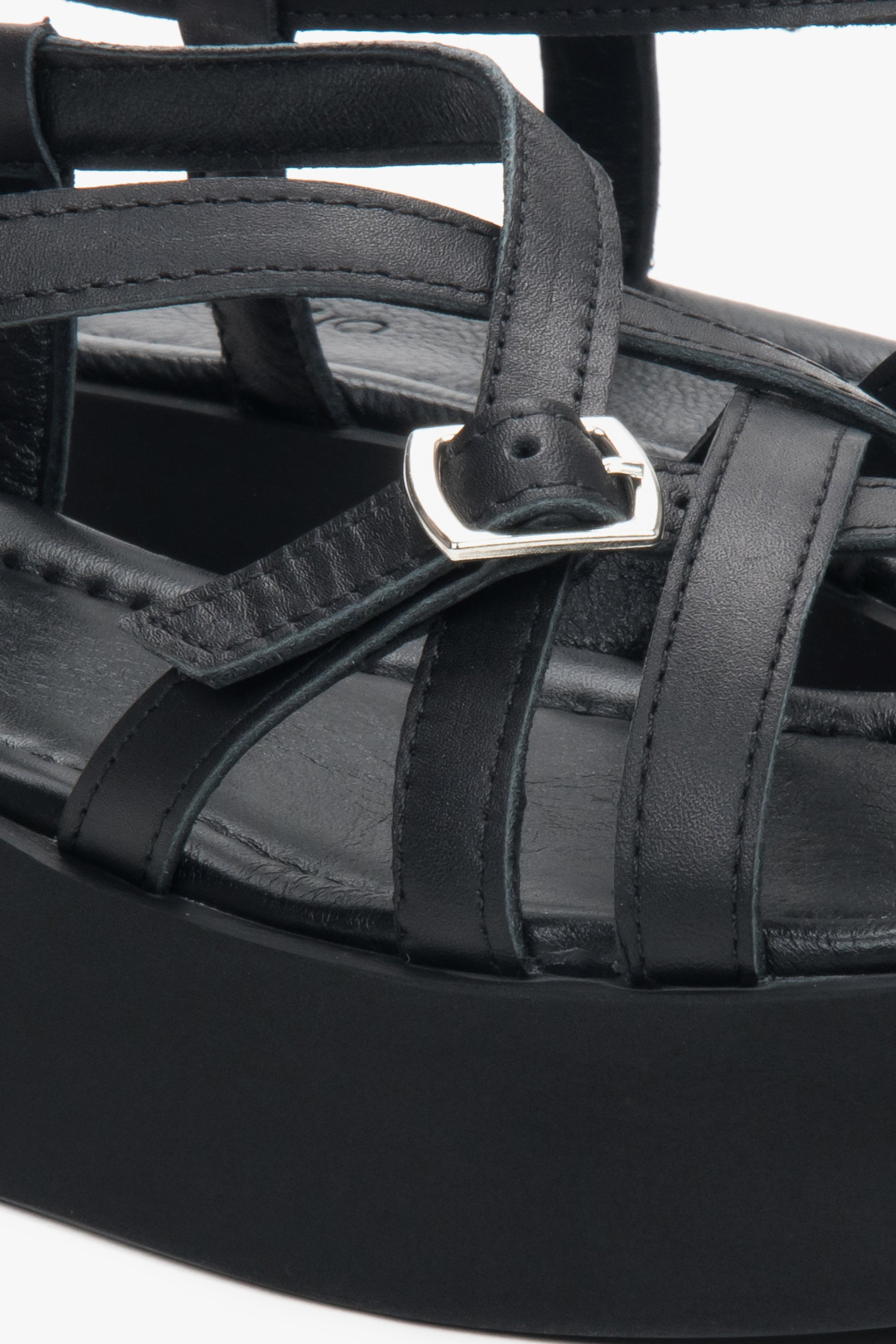 Detailaufnahme der silbernen Schnalle und der Lederriemen an den schwarzen Plateau-Sandalen