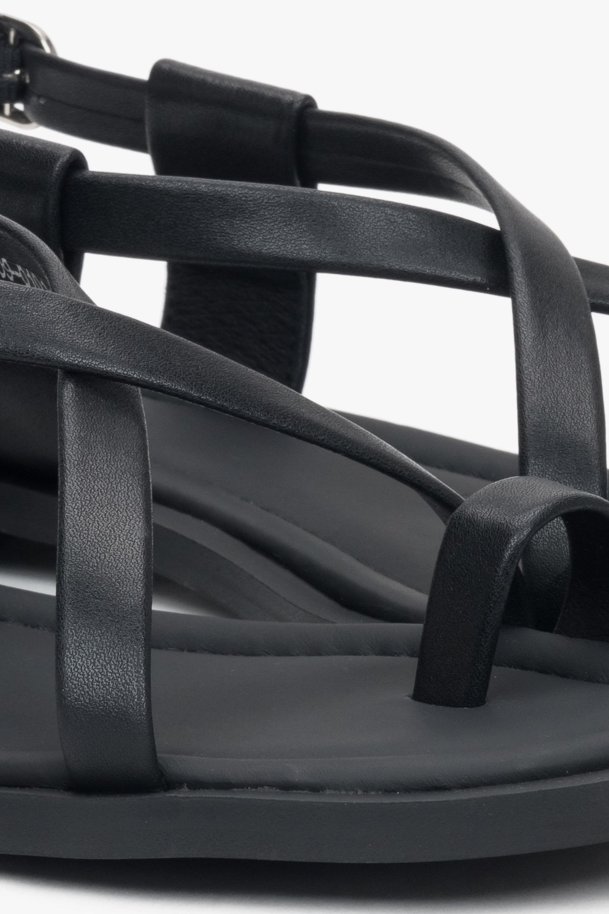 Nahaufnahme der dekorativen Zehenschlaufe und Riemen der schwarzen Damen-Sandalen.