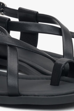 Nahaufnahme der dekorativen Zehenschlaufe und Riemen der schwarzen Damen-Sandalen.