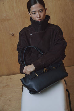 Kampagnenbild eines Models, das die schwarze Ledertasche elegant über der Schulter trägt