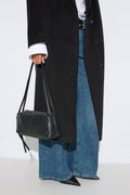 Stilvolle Lifestyle-Aufnahme eines Models im langen schwarzen Mantel, weiten Jeans und mit der schwarzen Schultertasche aus italienischem Echtleder.