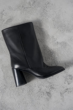 Atmosphärische Aufnahme der schwarzen Leder-Stiefelette mit weitem Schaft und Karree-Spitze auf grauem Untergrund