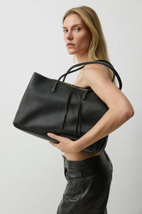Kampagnenaufnahme des Models mit schwarzer Damen-Tote-Bag aus Echtleder unter dem Arm