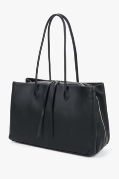 Schräge Frontalansicht der schwarzen Damen-Handtasche mit markanten Lederbändchen am Reißverschluss