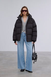 Model präsentiert die offene schwarze Winterjacke im Loose-Fit zu hellen Jeans