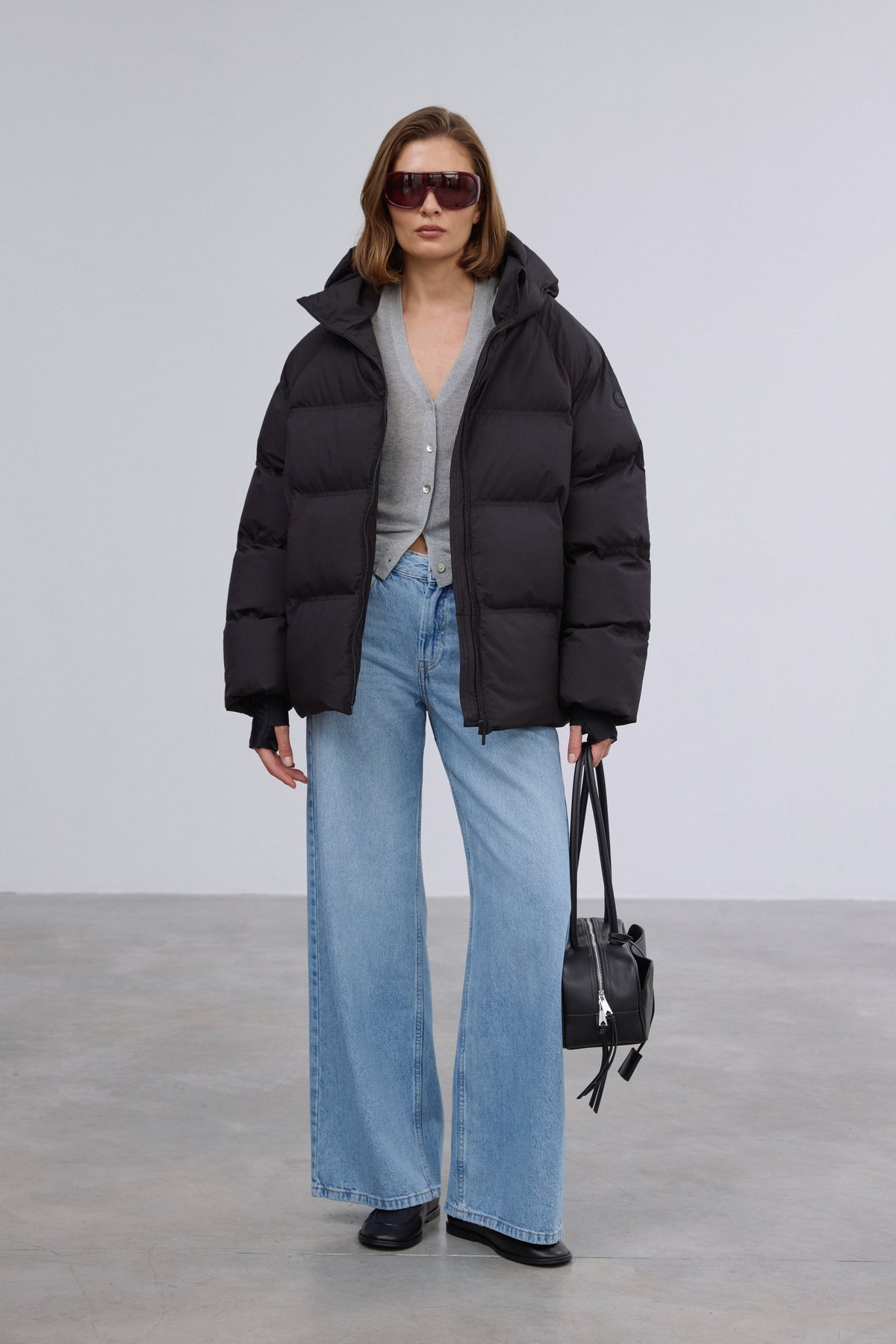 Model präsentiert die offene schwarze Winterjacke im Loose-Fit zu hellen Jeans