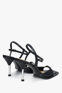 Rückwärtige Schrägansicht der schwarzen Stiletto-Sandaletten mit Fesselriemchen und glänzendem Absatz