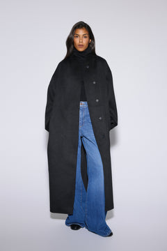 Frontalansicht des Models im offenen schwarzen Kamelhaarmantel, kombiniert mit Rollkragenpullover und Flared Jeans