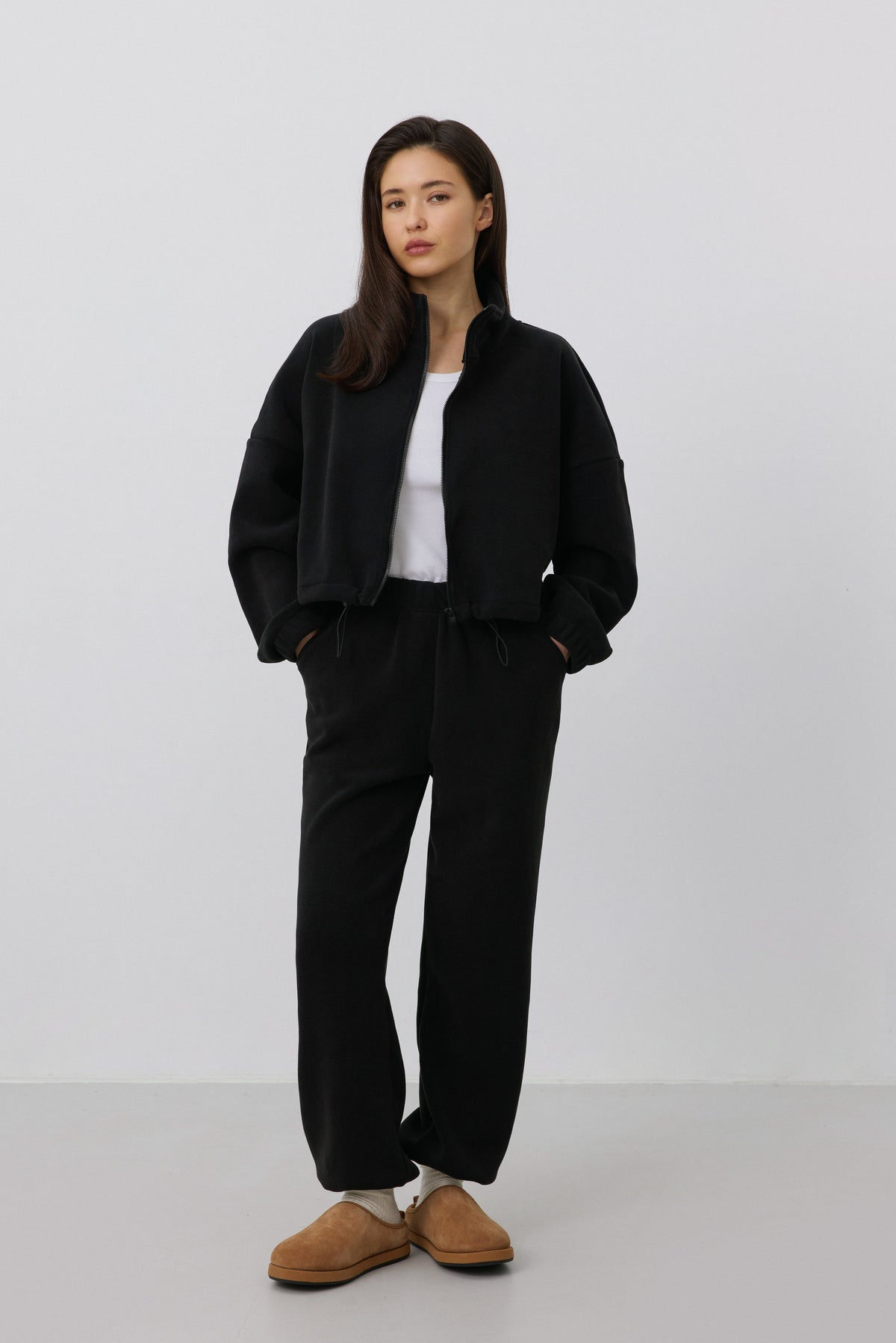 Frontalansicht des Models im schwarzen Damen-Fleece-Set mit entspanntem Loose Fit und braunen Hausschuhen