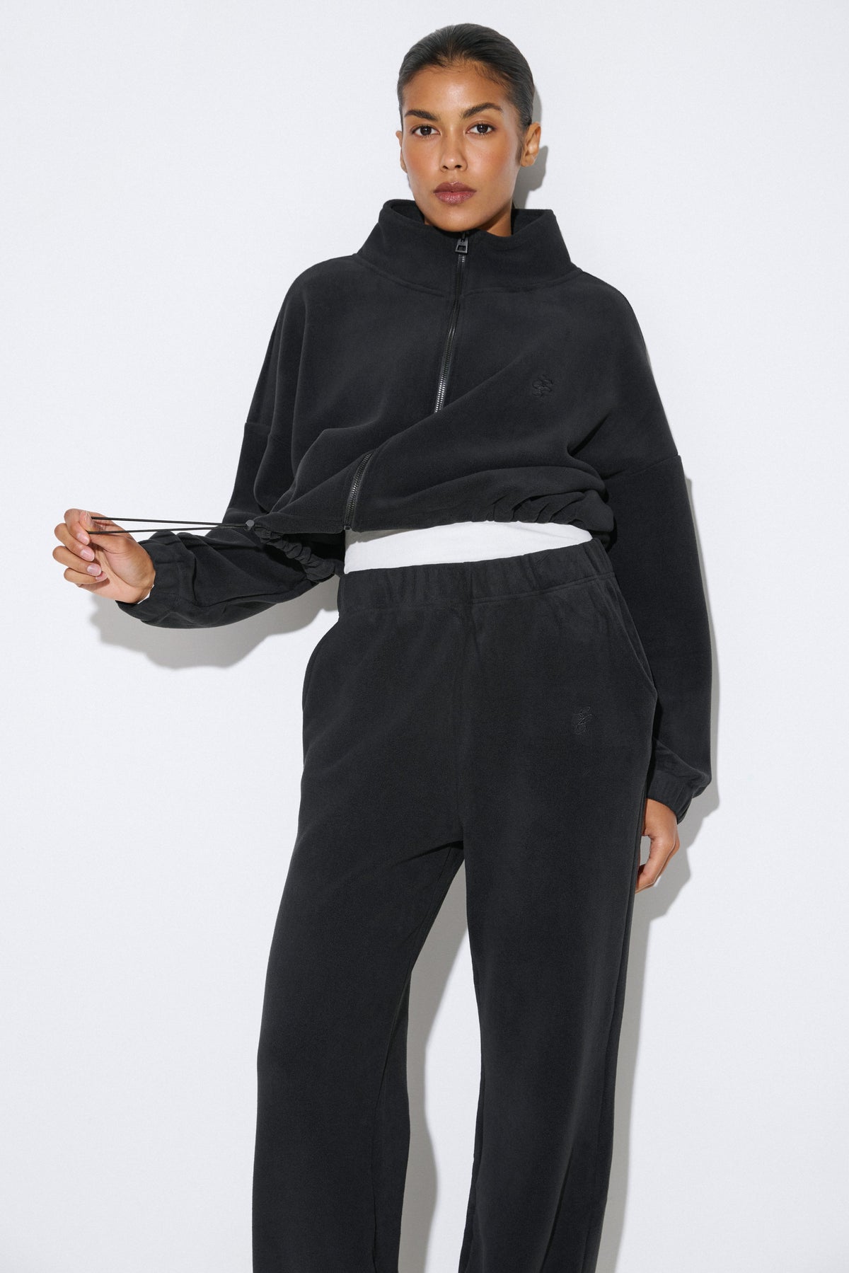 Lifestyle-Aufnahme des Models im schwarzen Fleece-Set, präsentiert mit einem lässig umgebundenen blauen Akzent