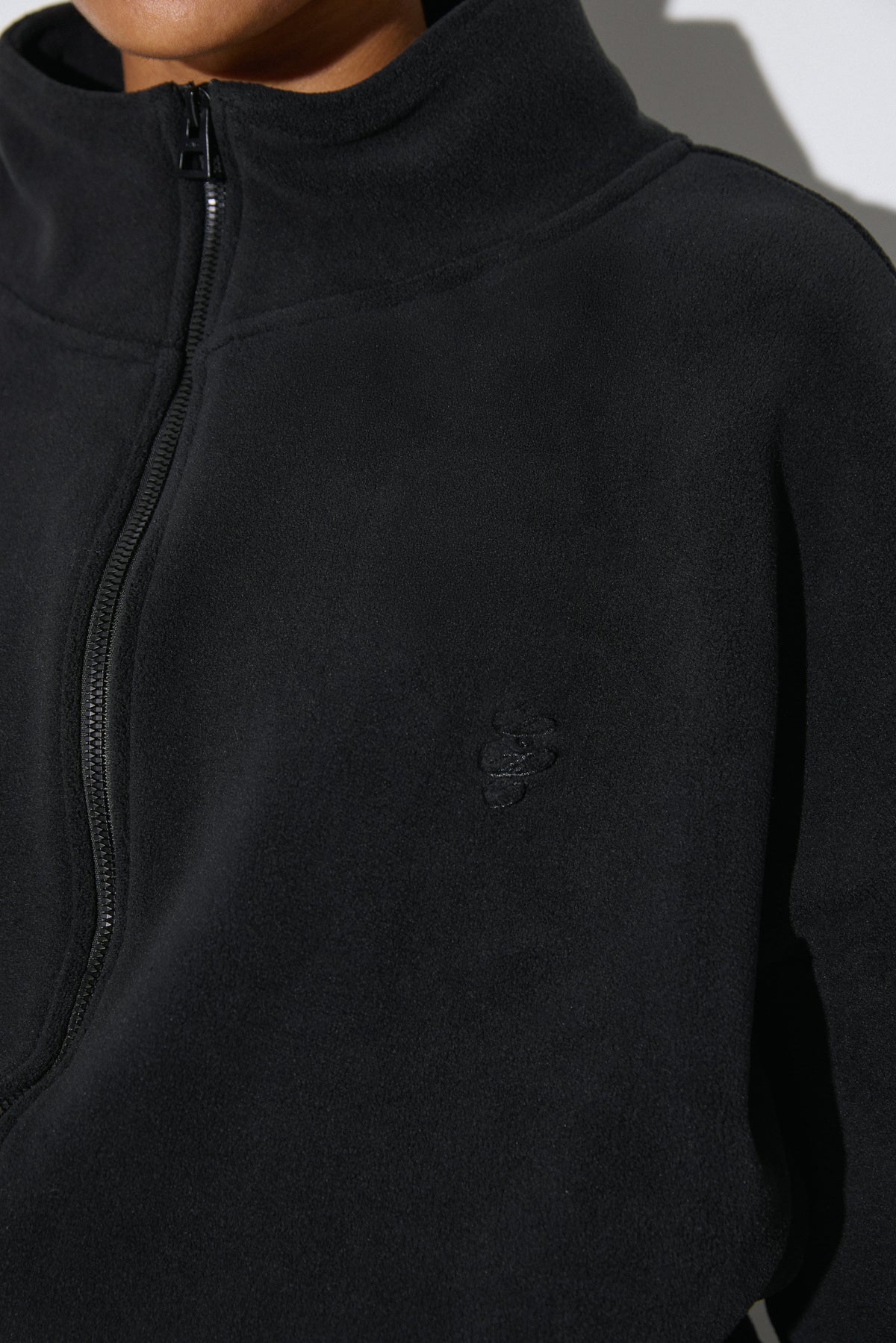 Detailaufnahme der schwarzen Fleece-Jacke mit Reißverschluss, Stehkragen und einem dezenten Estro-Logo auf der Brust
