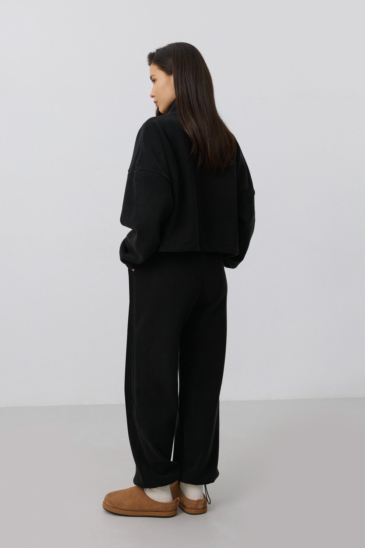 Rückansicht des Models in dem schwarzen Fleece-Set, die den lässigen Schnitt der Hose und des Oberteils betont
