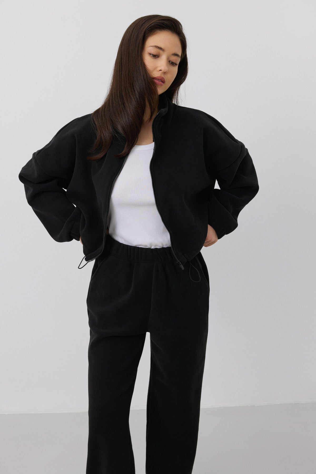 Frontalaufnahme mit geöffnetem schwarzen Fleece-Oberteil, lässig über einem weißen Basic-Shirt getragen