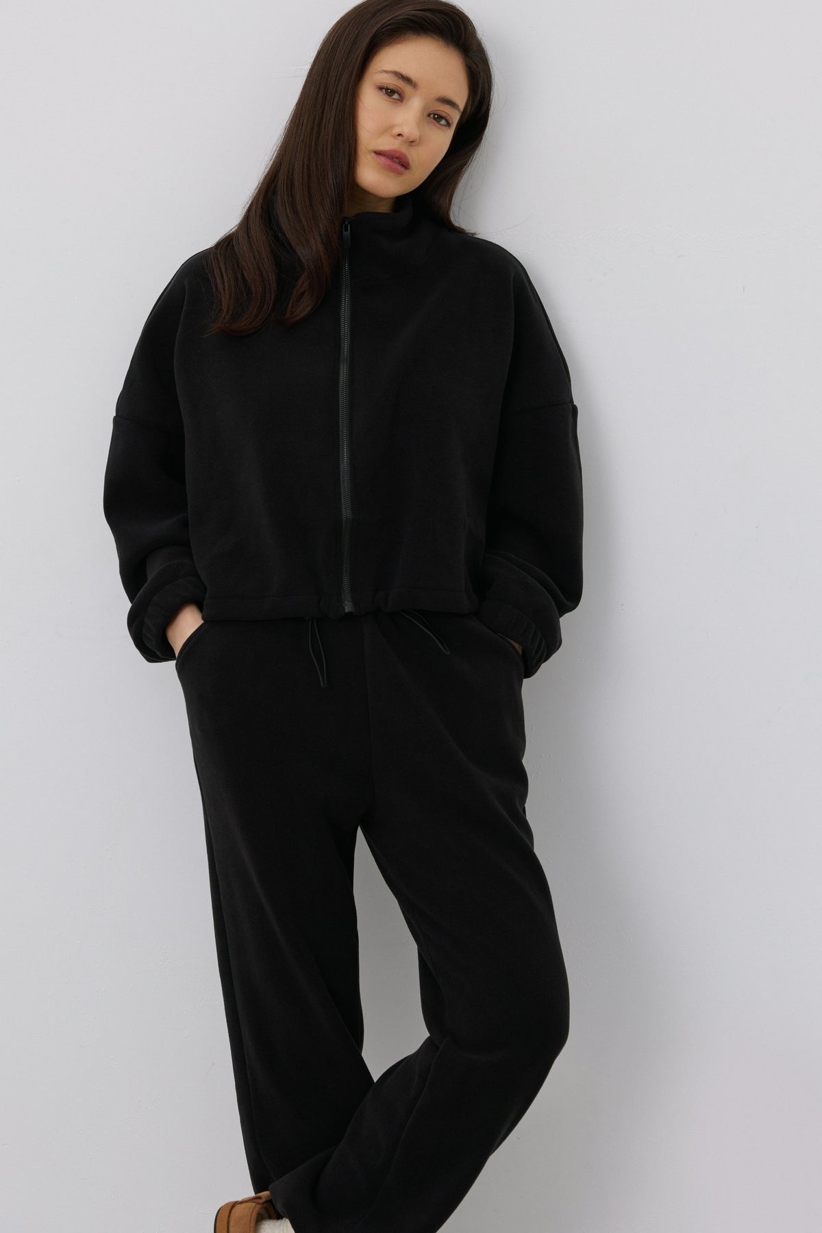 Leicht seitliche Ansicht des Models, das die Hände entspannt in den Taschen der schwarzen Fleece-Hose hält