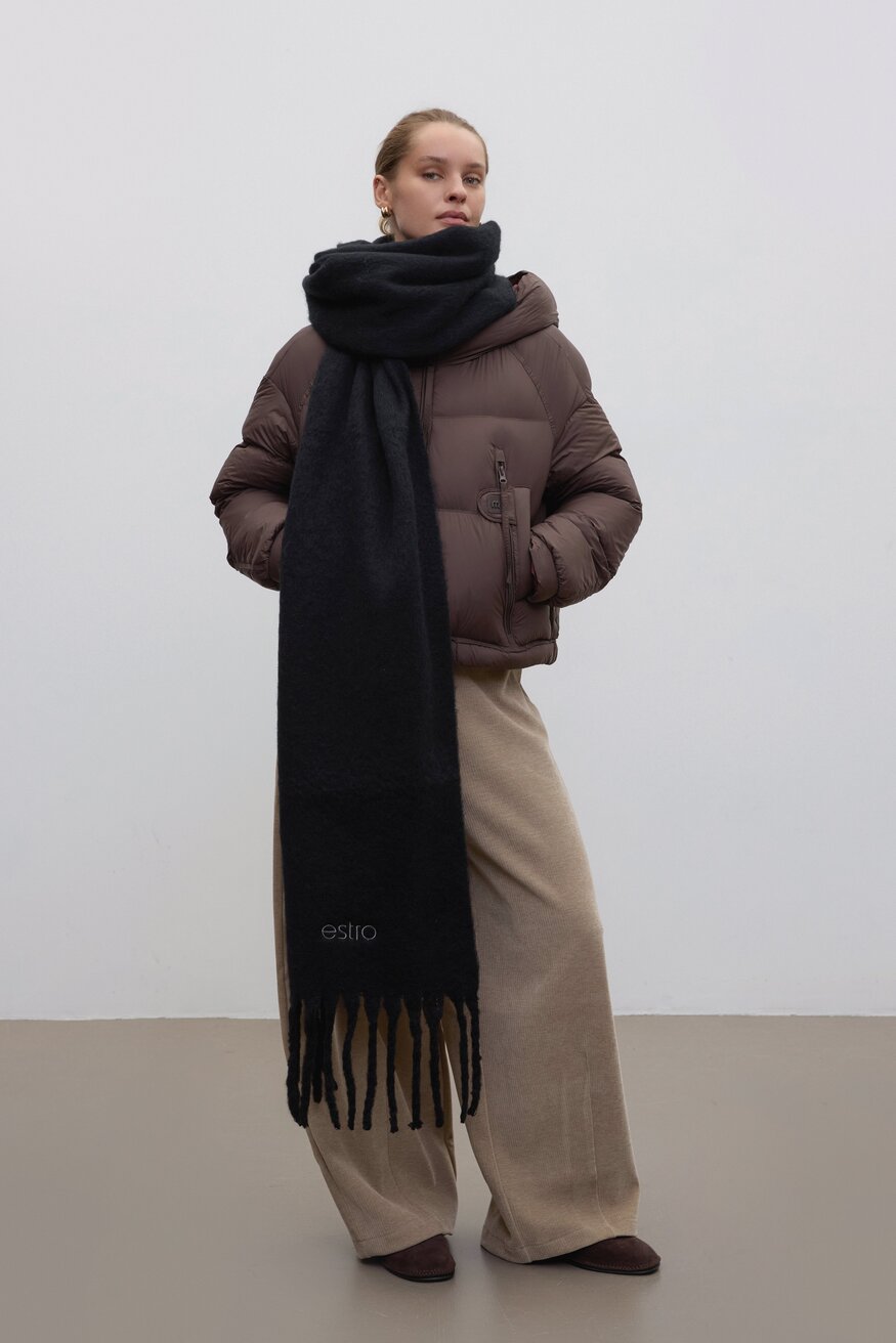 Lifestyle-Aufnahme eines Models in brauner Winterjacke und beigefarbener weiter Hose, das den voluminösen schwarzen Schal mit Fransen von Estro trägt