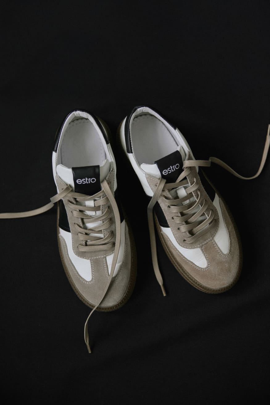 Weiße und graue Sneaker aus Naturleder und Velours – Präsentation von oben auf schwarzem Hintergrund.