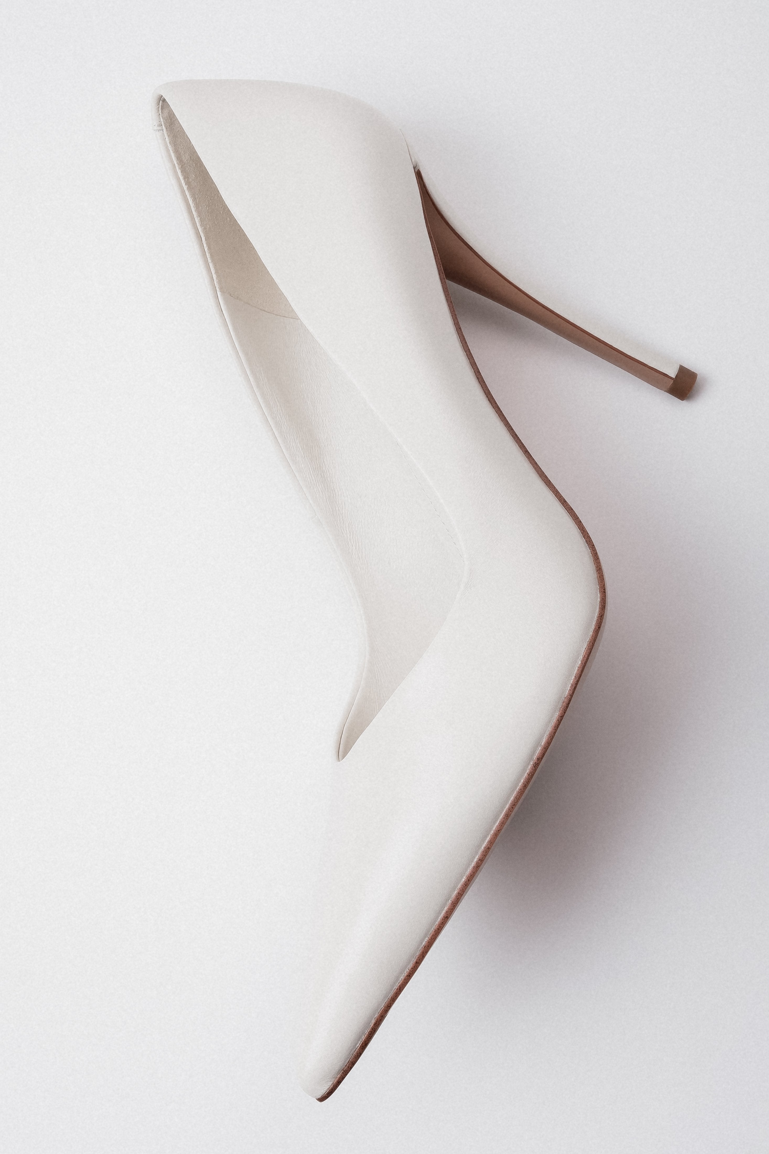 Weiße Damen-Pumps aus Echtleder in künstlerischer Seitenansicht mit spitzer Schuhspitze
