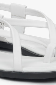 Nahaufnahme der dekorativen Zehenschlaufe und Riemen der weißen Damen-Sandalen.