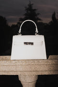 Weiße Damen-Handtasche von Estro auf steinerner Balustrade vor dunklem Hintergrund