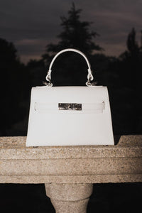 Weiße Damen-Handtasche von Estro auf steinerner Balustrade vor dunklem Hintergrund