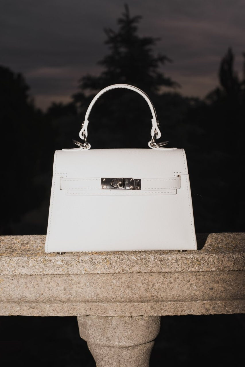 Weiße Damen-Handtasche von Estro auf steinerner Balustrade vor dunklem Hintergrund