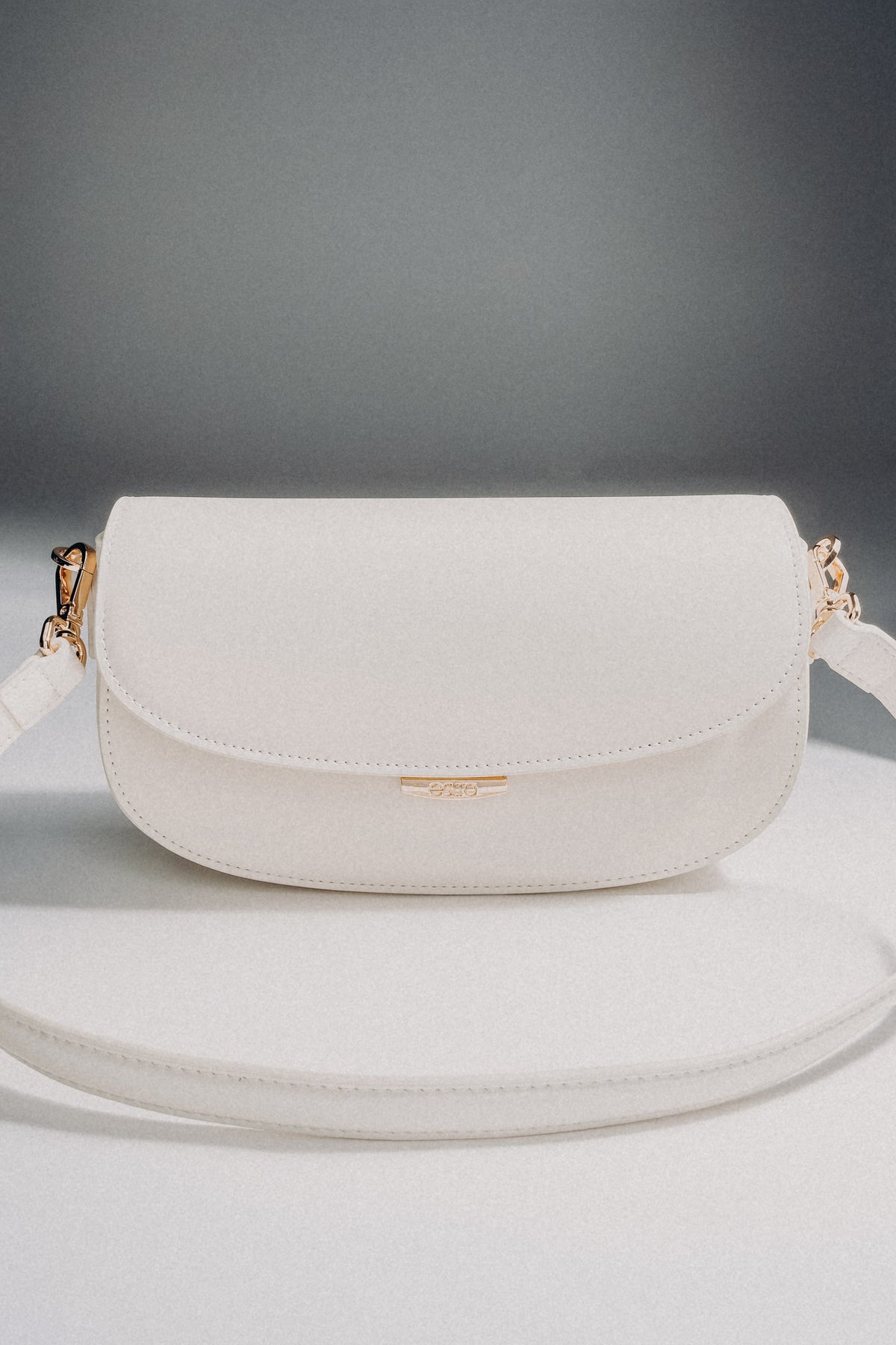 Weiße Damen-Schultertasche aus Leder in Hufeisenform auf grauem Hintergrund.