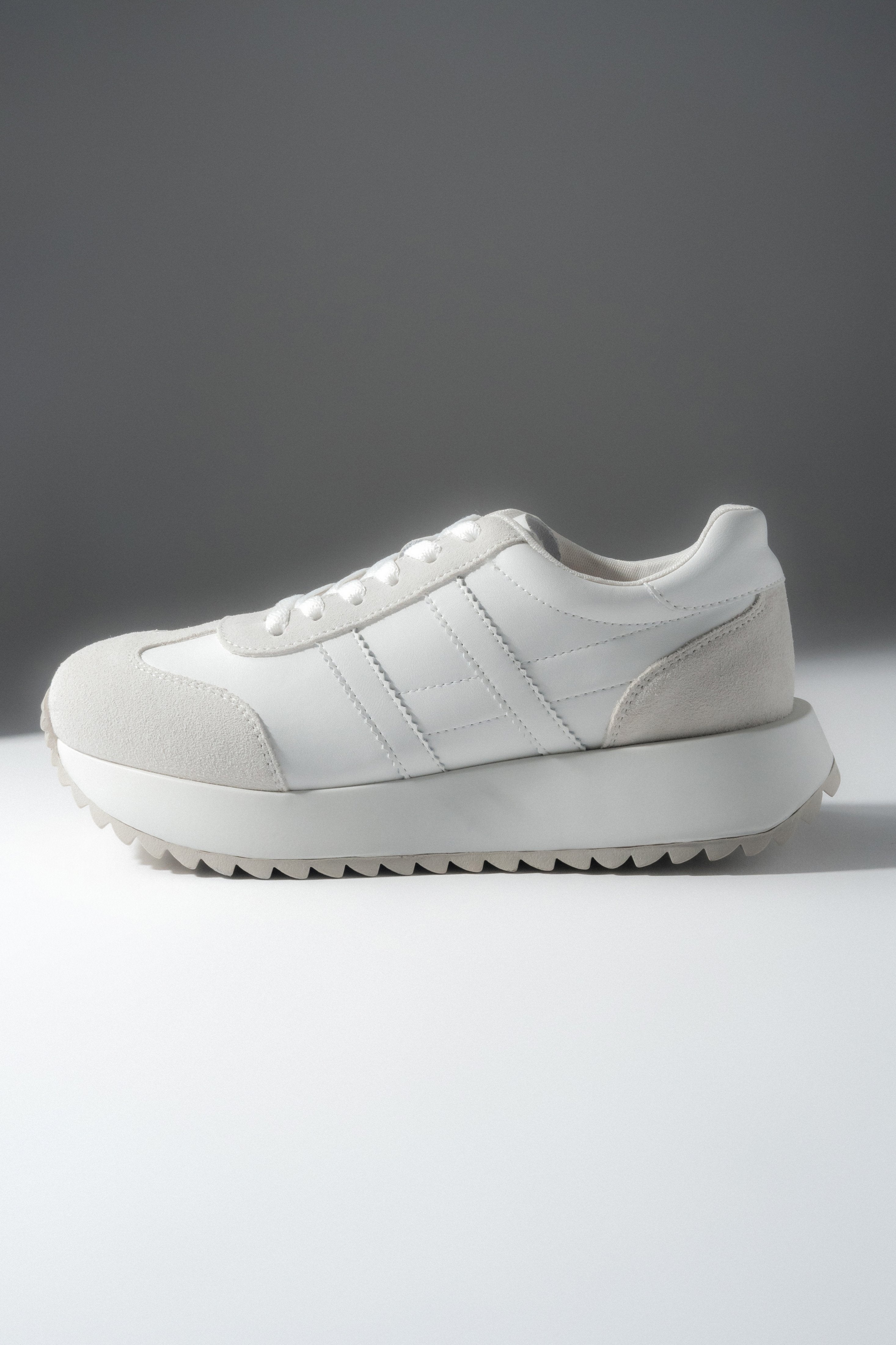 Leicht schräge Seitenansicht des weißen Sneakers mit Schnürung.