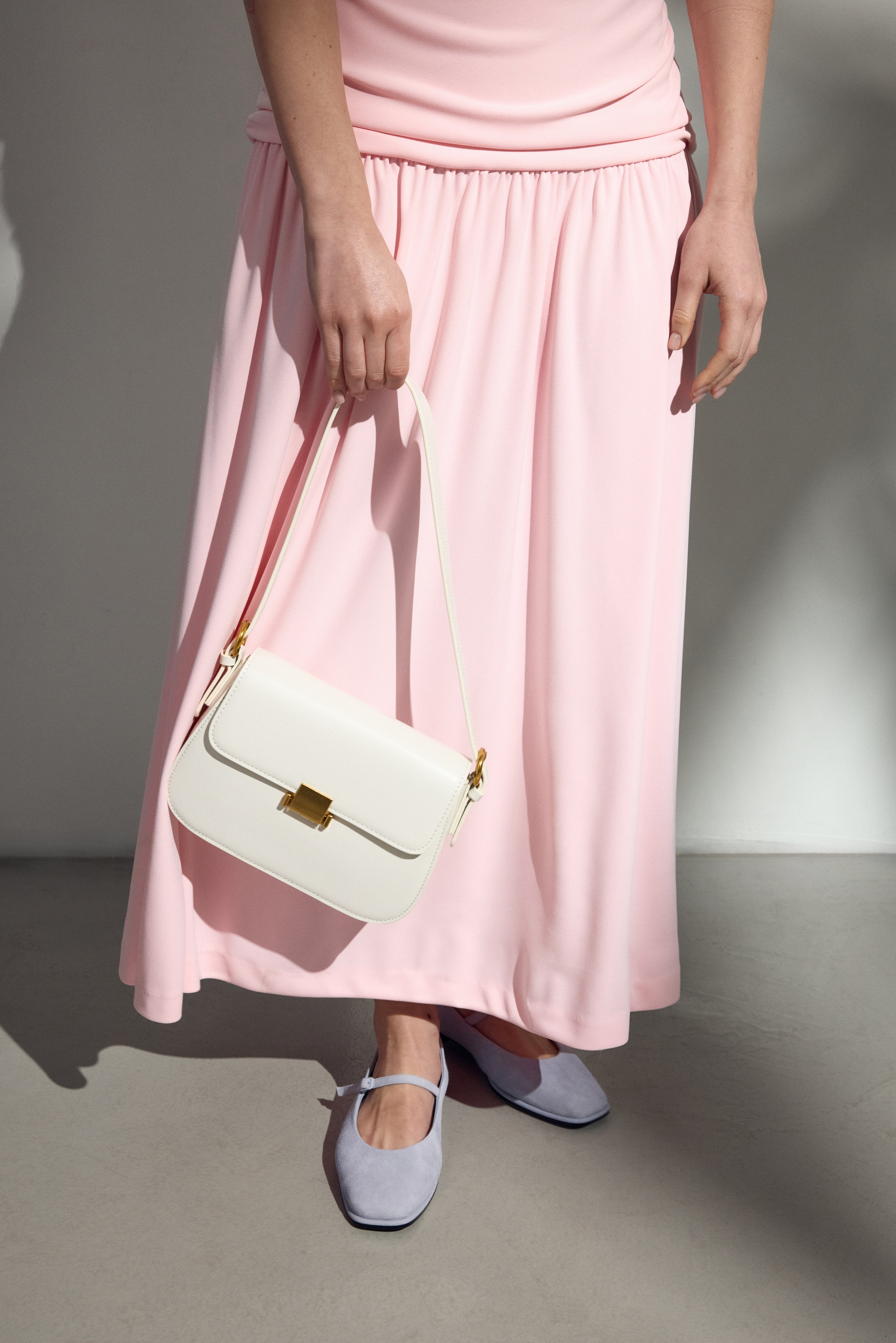 Model im rosa Kleid trägt die elegante weiße Schultertasche von Estro.