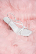 Weiße Slip-On-Sandalette mit feinen Riemchen, elegant präsentiert auf rosafarbenem Kunstfell